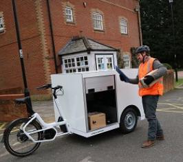A man wearing an orange hi-vis jacker making deliveries using a white E-cargo bike